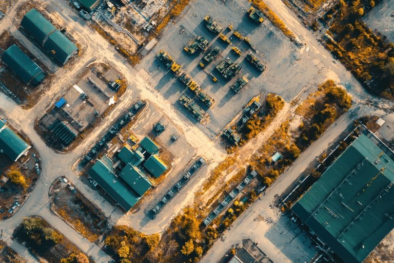 A Bird's-Eye View: Military Base Under Construction, Rows of Vehicles Aligned in Parking Lots, Buildings with Green Roofs, and a Dusty, Sandy Terrain