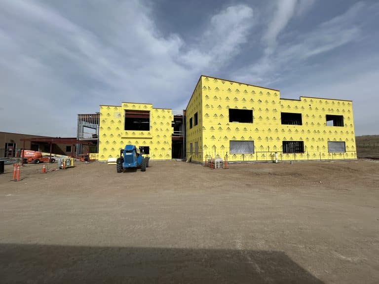 Construction progress at Jenkins Middle School showing new building addition with yellow exterior sheathing, window openings, and equipment on site in Colorado Springs
